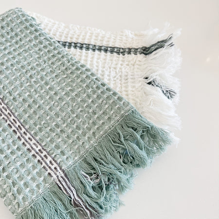 Set of 2 Rosemary waffle hand towels. Sage green towel with fine white and grey stripe with fringe ends. White waffle towel with sage green and grey stripe and fringe ends. Measures 28" x 18". 100% cotton,