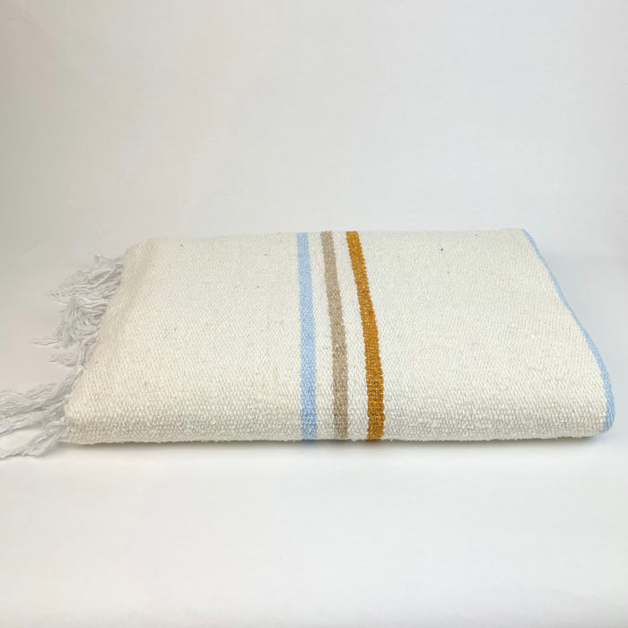 The Sunny Daze Throw is woven from 100% post consumer fibers. Sustainability meets modern California style. Natural cream ground with blue, tan and rust stripes is finished with hand twisted fringe. Measures 48" x 73"