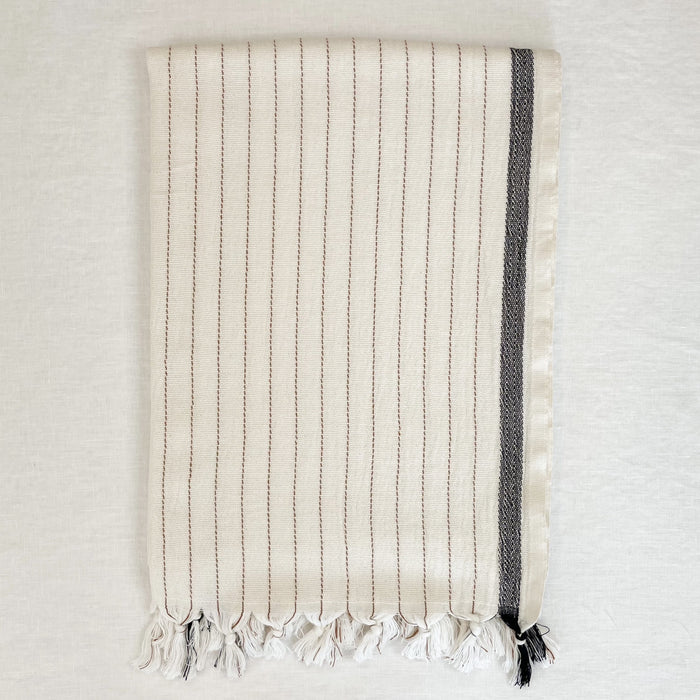 The Monterey Bath Towel is a luxurious over sized towel worthy of a spa. Made in Turkey on traditional looms in 100% cotton.  Unbleached cream color towel  with terra cotta pinstripes and a black border. Hand knotted tassels finish off each end. Measures 37"W x 74"L.