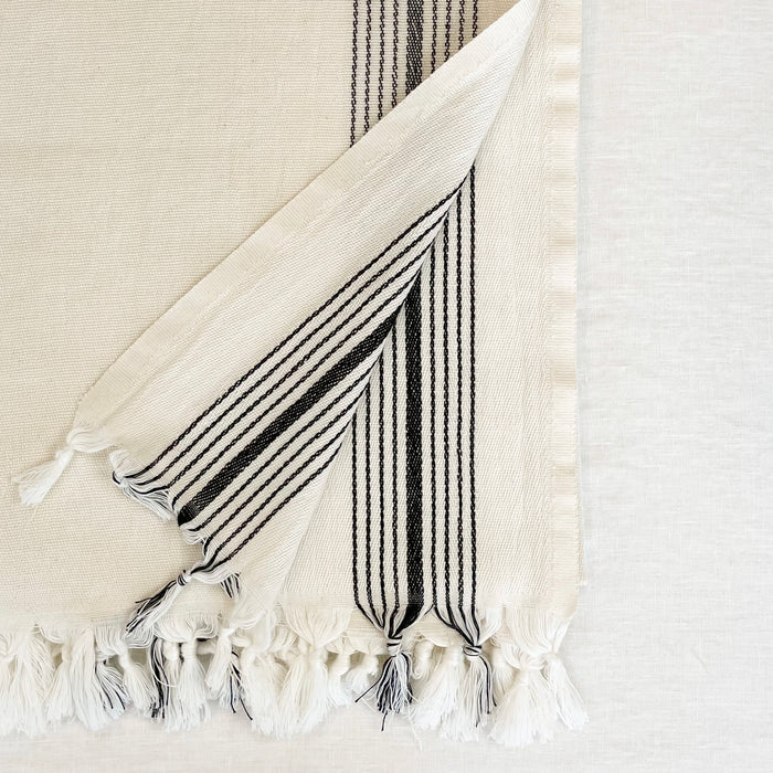 The Malibu Bath Towel is luxuriously oversized. Measures 33" x 74" L. Made in Turkey on traditional looms in 100% cotton. The unbleached cotton towel is framed with a cluster of thin black stripes on each side. Hand knotted tassels finish off each end.