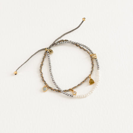 Isabelle double strand bracelet. One strand features tiny seed pearls and silver beads, the other strand has a fine gold chain woven through grey cord with delicate semi precious stone charms. Adjustable, one size fits most. Hand crafted by TAI Jewelry.