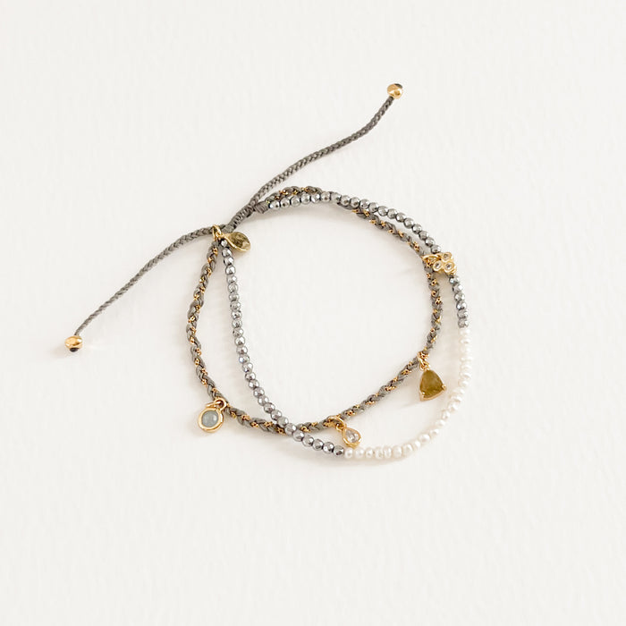 Isabelle double strand bracelet. One strand features tiny seed pearls and silver beads, the other strand has a fine gold chain woven through grey cord with delicate semi precious stone charms. Adjustable, one size fits most. Hand crafted by TAI Jewelry.