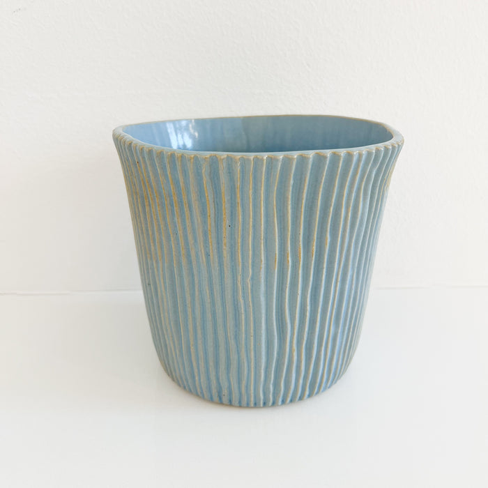 Pale blue carved stoneware planter. Vertical hand carved lines create texture highlighted by the soft blue glossy glaze. Measures: 7.75" diameter, 6.25" high.