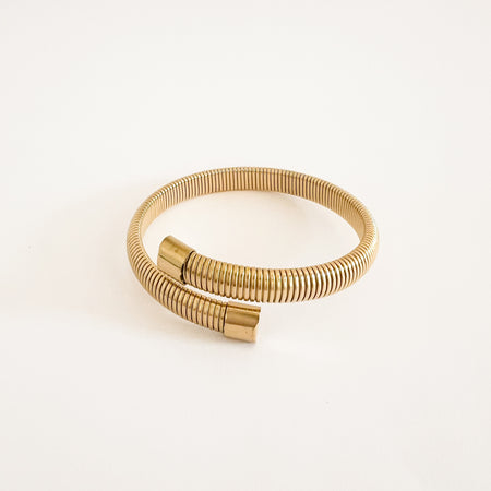 Neelie coil wrap bracelet. Flexible gold coil wraps around the wrist with open ends finished with end caps. Water, sweat and tarnish resistant jewelry. Made of hypoallergenic stainless steel with gold plating by Ellie Vail. 7" circumference, .24" coil width.