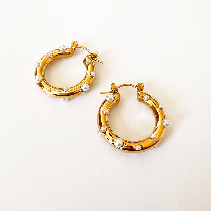 Nicoletta pearl hoop earrings by Ellie Vail. 1" round gold hoops with baby pearls embedded in the surface. Sweat, water and tarnish resistant. Made of marine grade stainless steel with gold plating and white pearls.