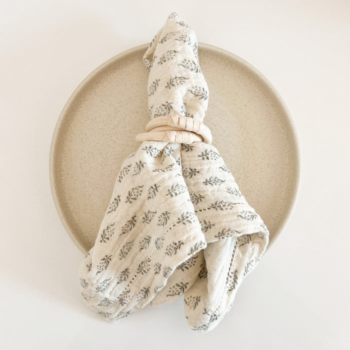 Pari woodblock napkin in unbleached cotton gauze with black woodblock floral print styled with rattan napkin ring and Mesa dinner plate. Boho chic table setting. Each sold separately.