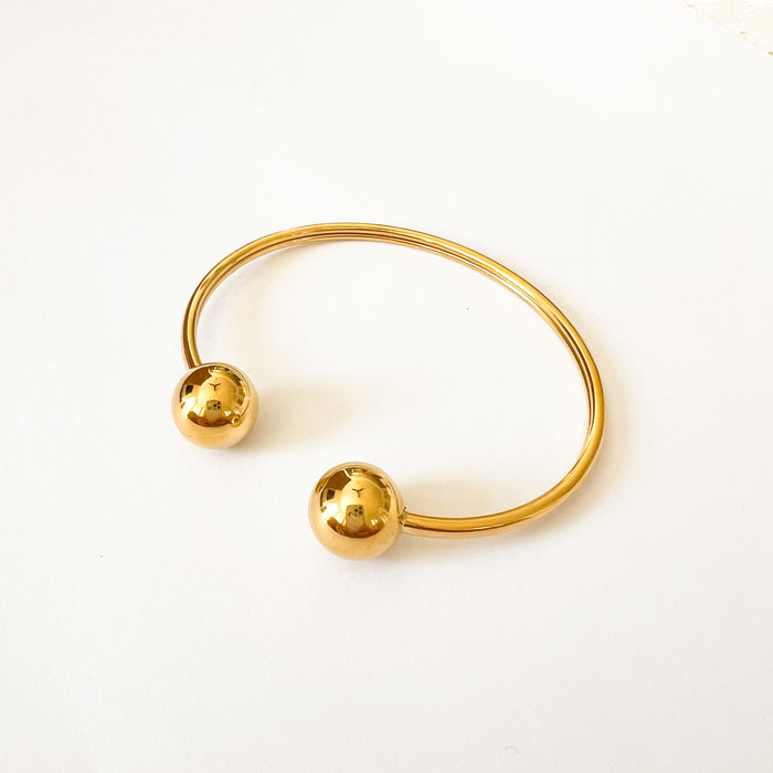 Talia bracelet by Ellie Vail. Slim open ended gold cuff with gold spheres on each end. 8" circumference. Sweat, water and tarnish resistant. Made of marine grade stainless steel with gold plating.