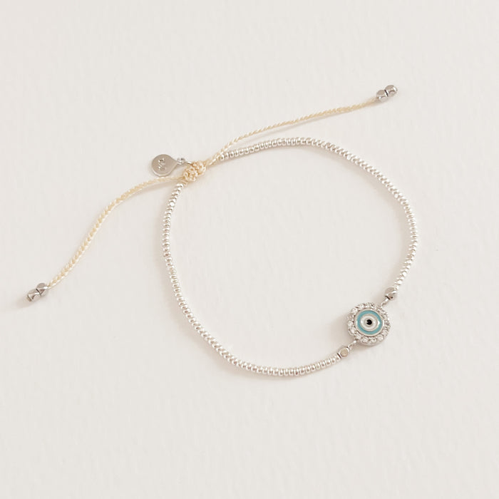 Ansel bracelet strung with tiny silver beads and featuring a CZ encrusted evil eye pendant. Pull cord adjuster. Hand crafted by TAI Jewelry.