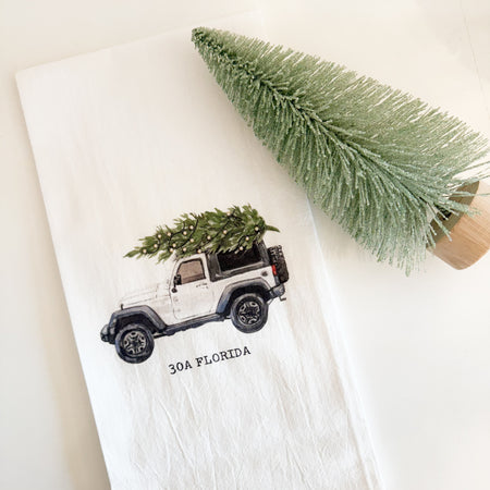 White cotton tea towel printed with image of a white jeep carrying a Christmas tree. Custom black "30A Florida" type. 21 x 28 inches.