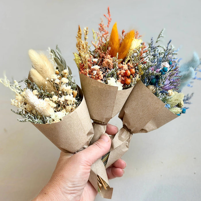 Bouquet of dried flowers wrapped in brown paper held by a hand against a plain background