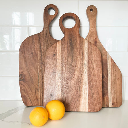 Scandi wood cutting boards. Three organic shaped cutting boards with rounded edges and handle with circular cut out. Made from natural Acacia wood. Subtle variations in color and grain will occur in each piece. Sold individually. Each piece varies slightly in shape. Approximate size 15" length, 8.5" width, .5" thick.