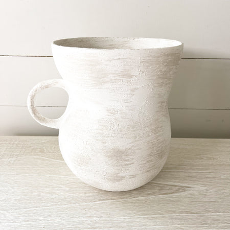 Pueble Vase. Rustic ceramic vase in a raw white glaze with undertones of sand. Rounded shape with wide top brim and rounded handle on one side. Hand crafted in Portugal. Measures 9.5" H x 8" diameter.