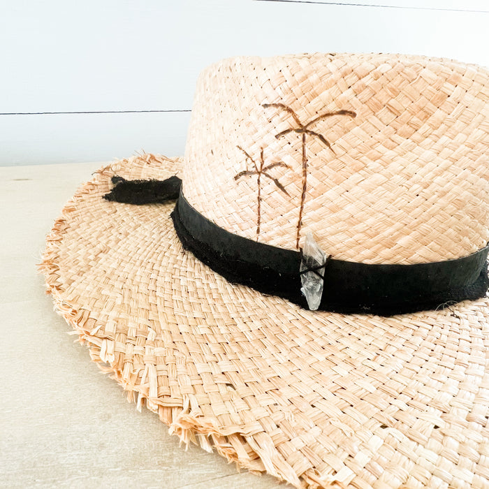 Boheme Raffia Hat with palm pyography on side of crown. Black suede and cotton gauze strips wrapped around crown with a clear quartz crystal sewn on. Handcrafted in Tulum Mexico.