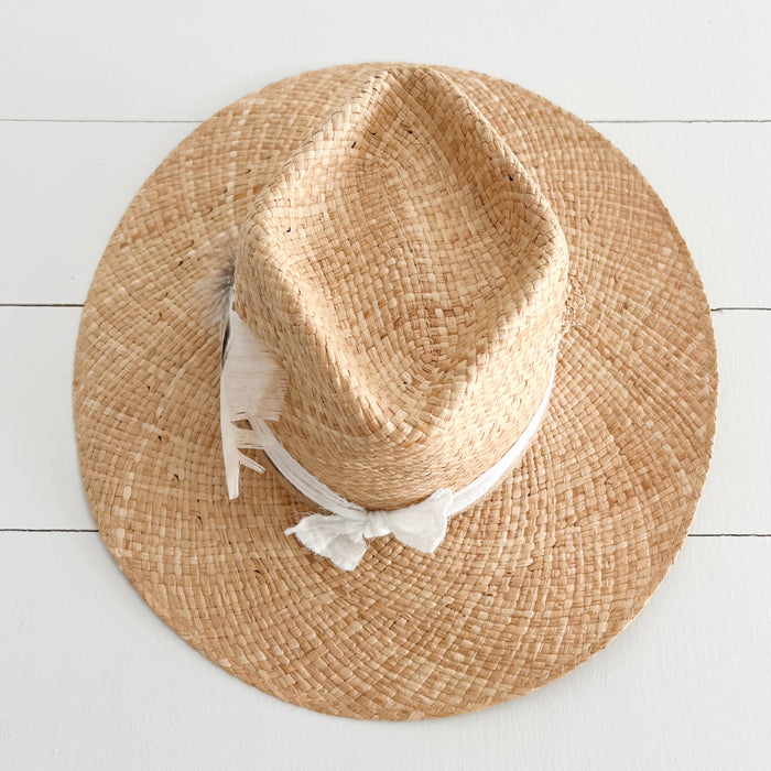 Top view of the Walk-About hat. Woven in natural palm fiber. A white cotton gauze strip is tied around crown with a bouquet of feathers stitched to the side.