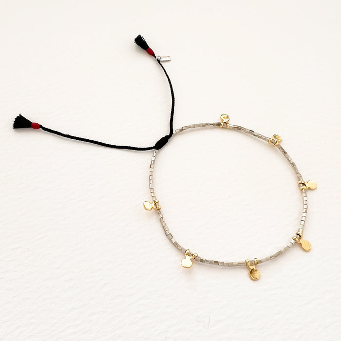 Delicate silver bead bracelet with tiny gold disc charms. Strung on finely braided black silk cord with mini tassel pull adjuster. Adjustable, one size fits most.