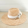 Walk-About hat woven in natural raffia. Crown is wrapped in a white cotton gauze strip and a natural braided jute strap. A bouquet of white and brown feathers are stitched to the side. Made by La Macarena Hats.