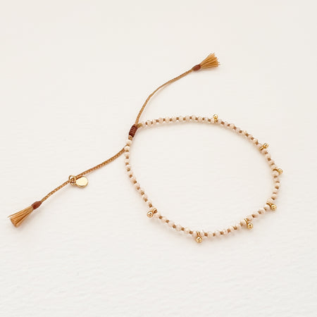 Adjustable bracelet with delicate faceted moonstone beads and mini gold charms. Hand knotted on ochre colored silk cord with pull adjuster finished with mini tassels. One size fits most.