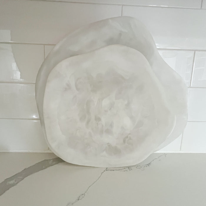 Amalfi serving platters in medium and large leaning on kitchen counter. Curvy organic shaped platters made in swirls of opaque and translucent white resin. Suitable for indoor/outdoor serving. Each sold separately. Hand wash only. Medium 12.5 x 11.75 inches. Large 15.25 x 13.25 inches.