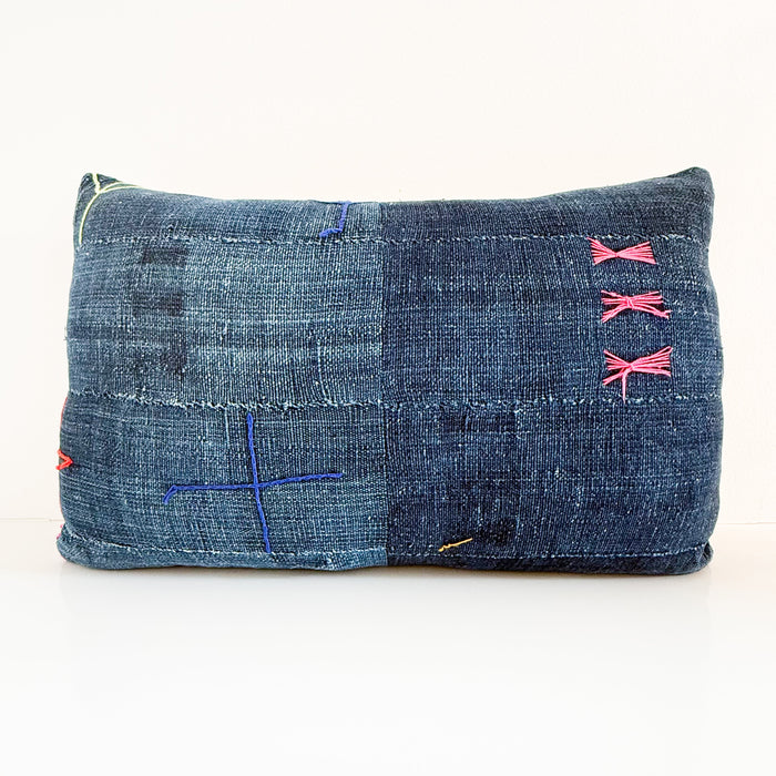 Indigo blue lumbar pillow made from authentic African mudcloth embroidered with playful motifs in pops of hot pink, cobalt blue, red and lime green. Backside is neutral linen. Measures 14 x 23 inches.