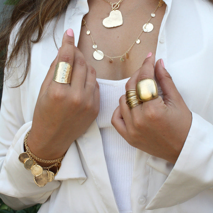 Close up shot of model wearing white shirt and hands up wearing gold rings featuring the Vionna Ring, the Cluster Wire Wrap Ring and the Lorabelle Dome Ring. Each sold separately.