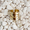 A textured gold wrap ring with a wide open band, resting on a bed of smooth white pebbles. Adjustable, fits size 7-9. 18k gold over brass.