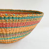 Close up of the Calypso basket bowl. Handwoven bowl shaped basket in stripes of orange, coral, turquoise and natural Abaca.