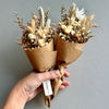 Hand holding two dried flower bouquets wrapped in brown paper against a gray background