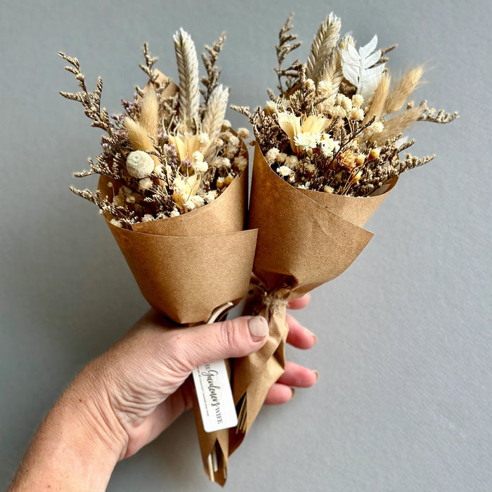 Hand holding two dried flower bouquets wrapped in brown paper against a gray background
