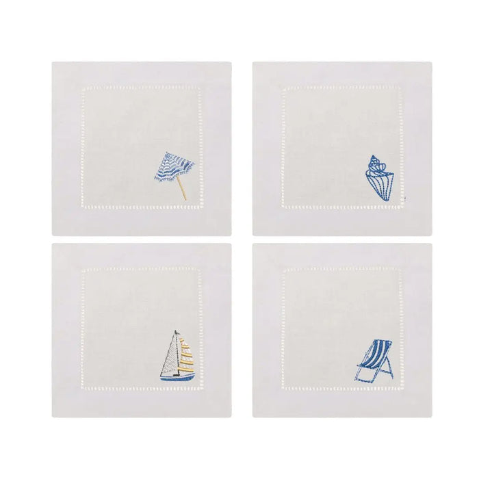Set of four white linen cocktail napkins with embroidered coastal designs on the lower right corner. Designs include a striped beach umbrella, a seashell, a sail boat and a striped beach chair. 6 inch square.