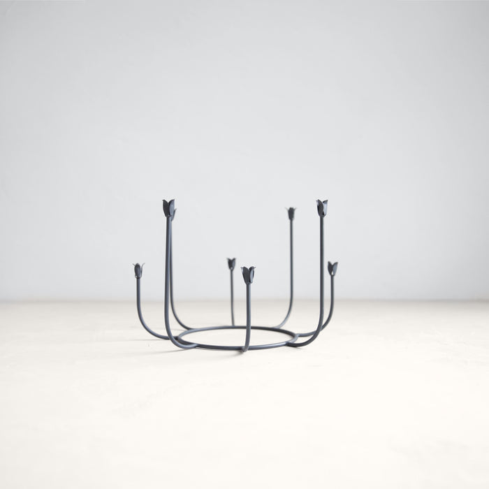 Round black wrought iron candelabra inspired by garden gates. Candle cups shaped like tulips. Holds eight slim taper candles. 10 inch diameter x 7 inch height.