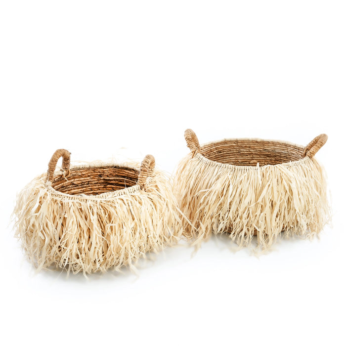 Two Boheme fringe baskets, one size medium the other large. Round belly baskets handwoven in Banana leaf with two handles and embellished with pale raffia fringe. Each sold separately.