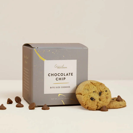 Box of chocolate chip cookies with two cookies and chocolate chips on a beige background