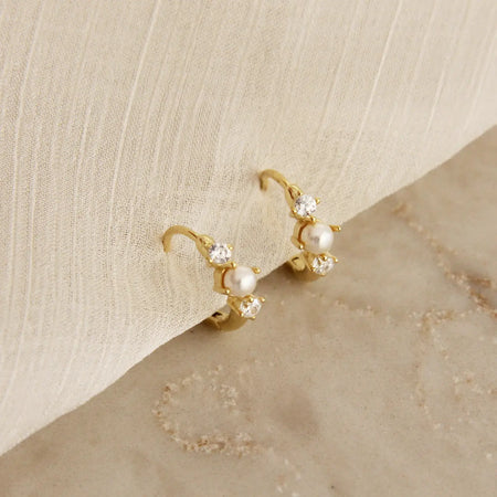 Delicate gold clicker hoops with a tiny white see pearl surrounded by two clear CZ stones. 18k gold plated over surgical steel. 11mm diameter.