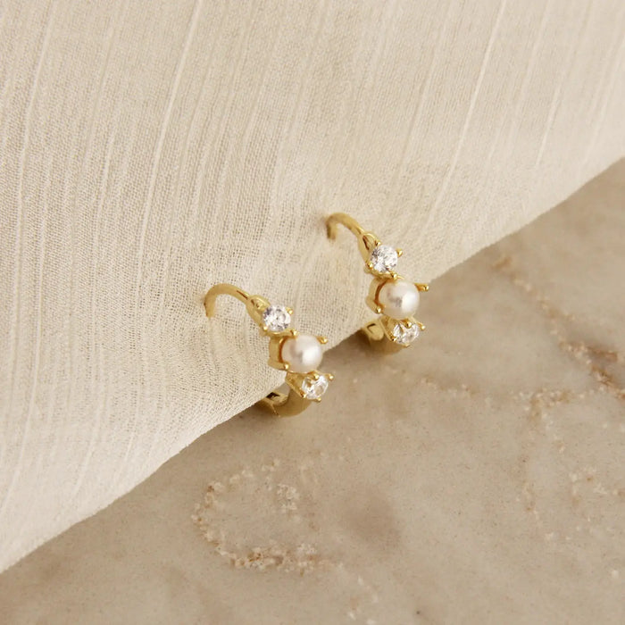 Delicate gold clicker hoops with a tiny white see pearl surrounded by two clear CZ stones. 18k gold plated over surgical steel. 11mm diameter.