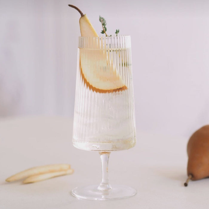 Clear fluted cocktail glass with a clear cocktail and pear garnish. Delicate tapered shape on top of a short stem. Measures 3" x 7". 12.85 oz/380ml capacity.