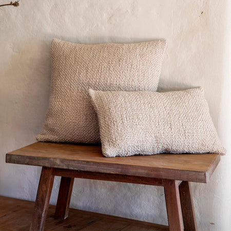 Two neutral textured boucle' pillows on a wooden bench against a textured plaster wall. Each pillow sold separately.