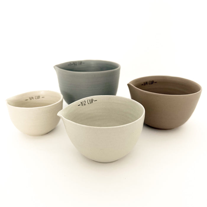 Set of four ceramic measuring cups in soft cream, taupe, terra cotta and mineral grey. Hand shaped spout and black lettering on edge to indicate measure.