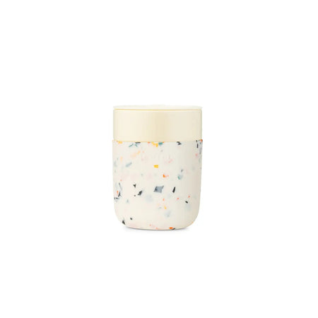 White ceramic tumbler with a cream and multicolor terrazzo silicon sleeve and a non-splash sipping lid. 12 oz capacity. Dishwasher and microwave safe.