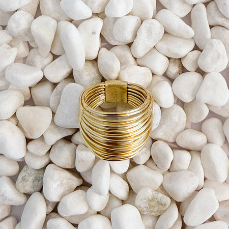 A cluster of gold wires wrapped into a ring on white pebbles. 18k gold over brass.