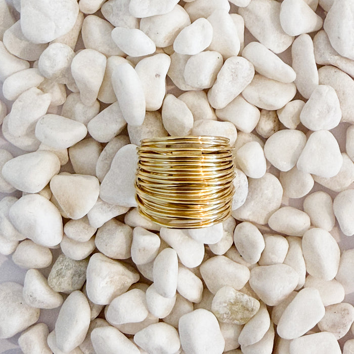 A gold ring made of a cluster of finely wrapped gold wires sitting on white pebbles. 18k gold over brass.