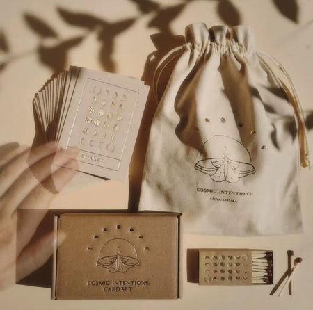 Cosmic Intentions Gift Set. Ivory linen drawstring bag contains a box set of 18 cosmic intentions cards and a Kraft matchbox printed with phases of the moon in gold foil. Cards are printed on natural high quality card with gold foil and contain an inspirational word and image.