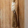 Close up detail of white cowrie shells crowning a natural raffia tassel. Hangs from a twisted raffia rope and wood bead.