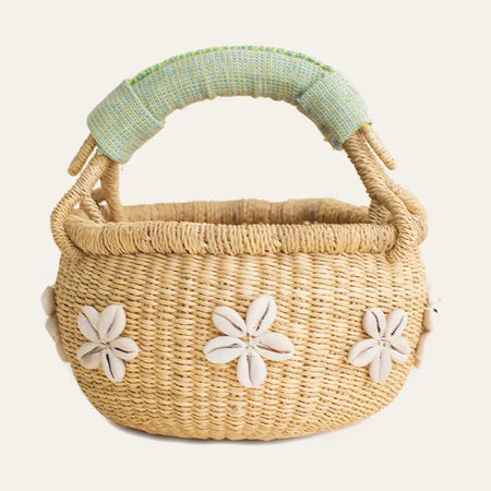 Woven basket with a pastel green handle and white  cowrie shells in the shape of a flower on white background. 7.5 x. 7.5 inches (3.5 inch handle drop).