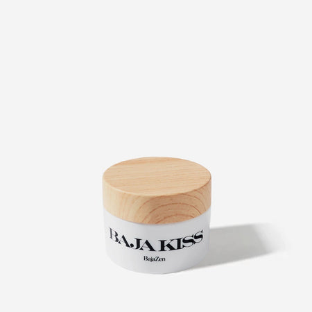 Baja Kiss lib scrub by Baja Zen. White jar with wood lid containing .75 oz/ 22ML  of lip scrub. Made of vitamin E rich almond oil and shea butter with raw sugar crystals to exfoliate.