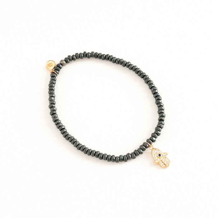 Stretch bracelet made with matte black Hematite beads (charcoal color) with a gold plated CZ encrusted Hamsa hand charm. Hand crafted by TAI Jewelry.