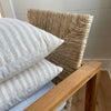 The White Sands Pillows shown stacked on a modern bohemian chair. Each pillow sold separately. Handwoven in a cream and sand stripe with subtle texture make this a relaxed and sophisticated layer to any neutral decor. Measures 20” x 20”.  Down insert included.