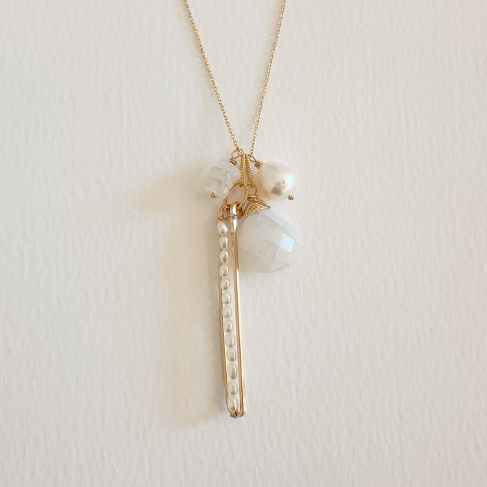 Close up of 4 charms on a 20" gold filled chain. A long strand of seed pearls on a fine gold threader, a faceted Moonstone, a mother of pearl and a stack of moonstones.