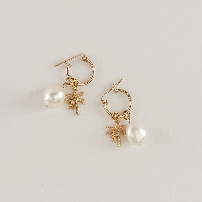Palm + Pearl Earrings. Two delicate gold filled hoops with clasp closure and charms. A golden palm tree with a tiny CZ crystal and a white Keish pearl charm. Hoop .5" diameter, 1" total length.