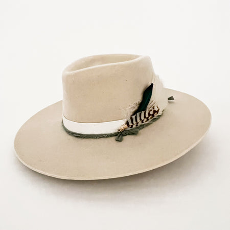 Earth Soul hat custom made by La Macarena Hats in Tulum Mexico. Finely crafted wool hat wrapped with a white leather strap, a sage green ribbon and adorned with hand embroidery, charred Palo Santo, a shimmering Moonstone and a small cluster of Turkey and Parrot feathers.