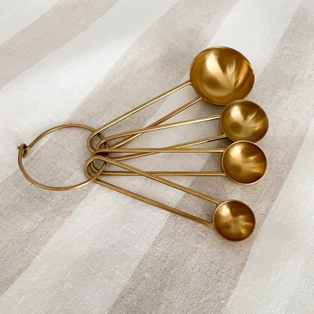 Set of essential brass measuring spoons by Hawkins NY. Made of stainless steel with a PVD brass coating. Sleek rounded handles on a brass ring. Includes 1 TBS, 1 tsp, 1/2tsp and 1/4tsp. Set comes in a drawstring muslin bag.